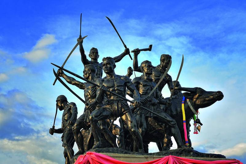 รูปปั้นวีรชนบางระจันถืออาวุธบนแท่น ตัดกับฟ้าสีคราม